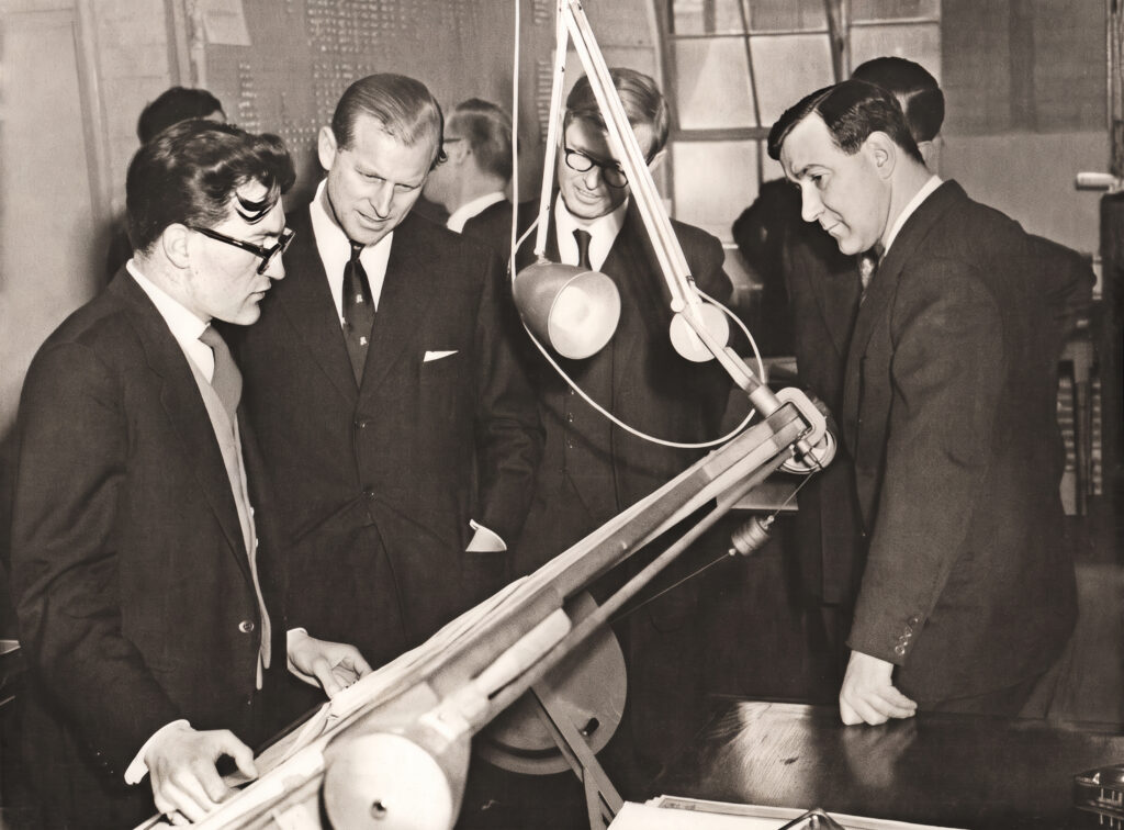 A designer at the drawing board with John Pinkerton to his left